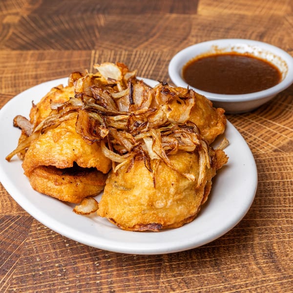 Fried dumplings topped with caramelized onions, served with a side of dark dipping sauce.