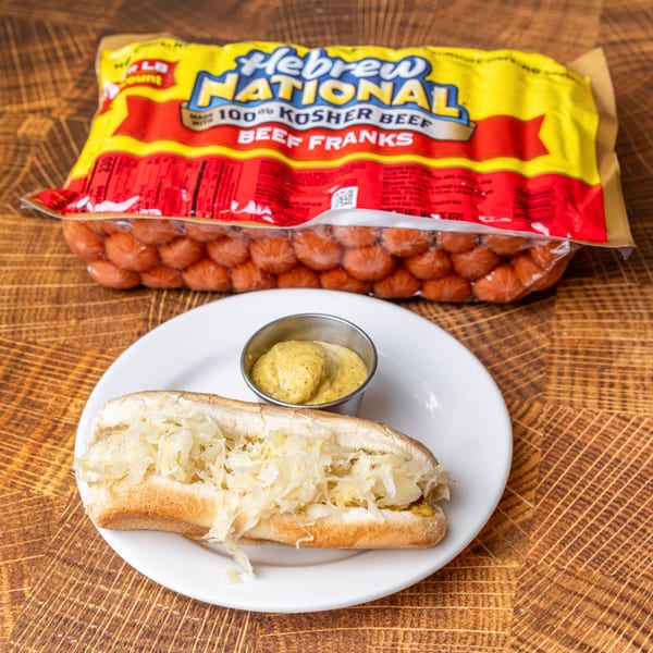 A hot dog with sauerkraut and mustard on a white plate, with a Hebrew National franks package.