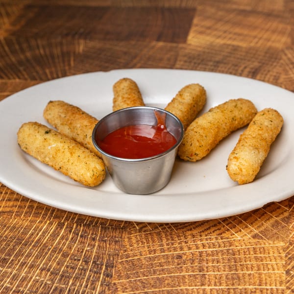 Six golden-brown mozzarella sticks arranged around a small metal cup of ketchup on a white plate.