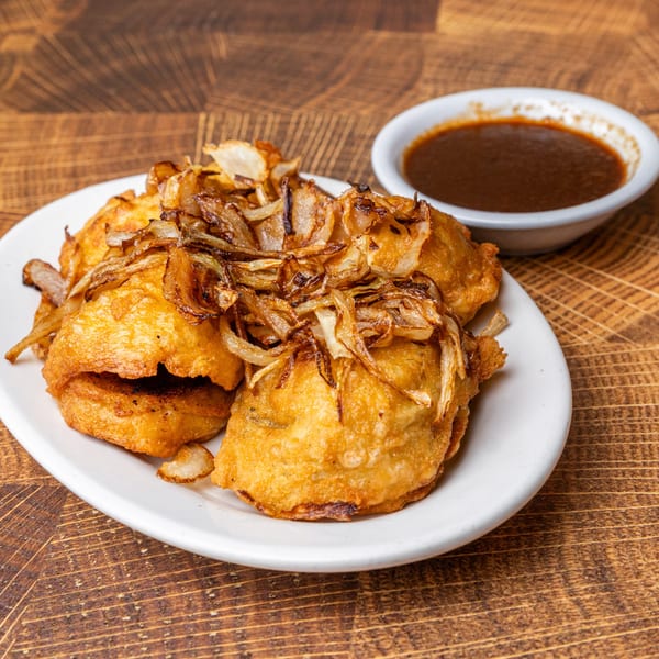 Fried pastrami dumplings topped with caramelized onions, served with a side of dipping sauce.