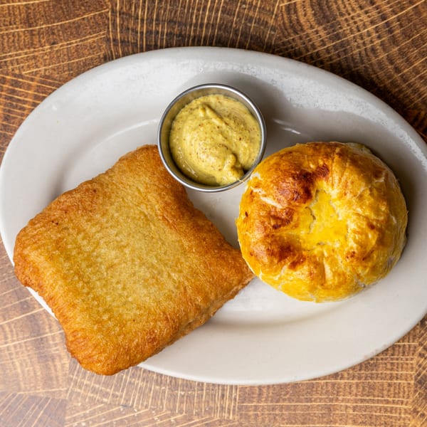Golden-brown fried potato latke, a round kugel, and a metal cup of mustard on a white plate.